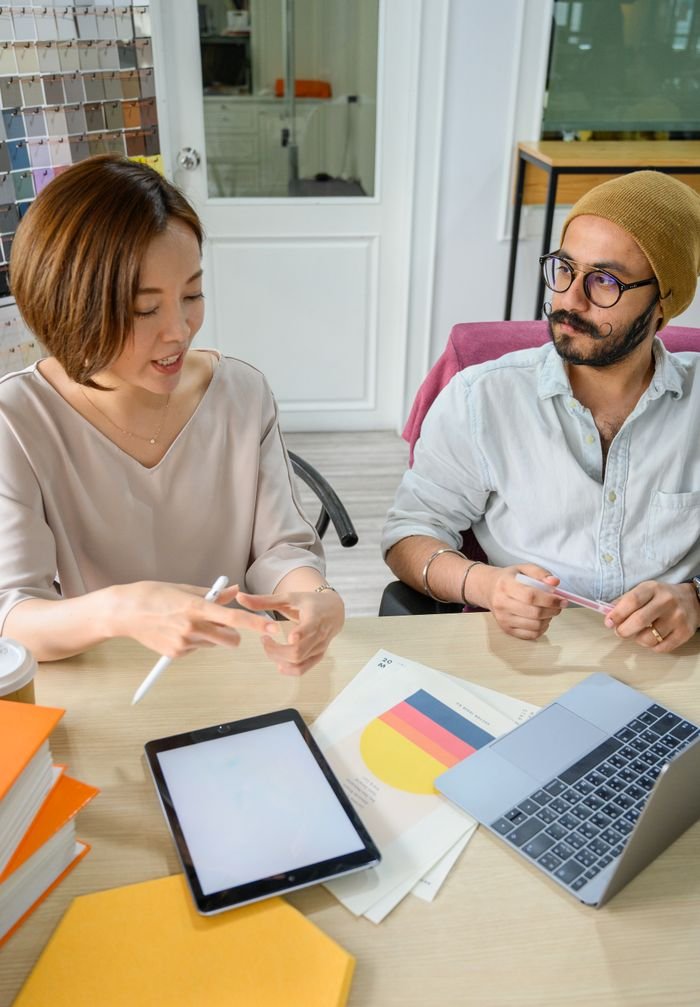 Two professionals discussing work at a desk with charts and technology.