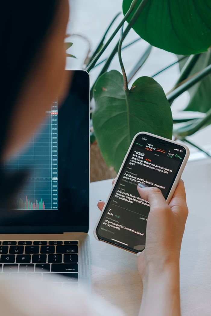 Person multitasking with financial graphs on laptop and smartphone, perfect for business concepts.